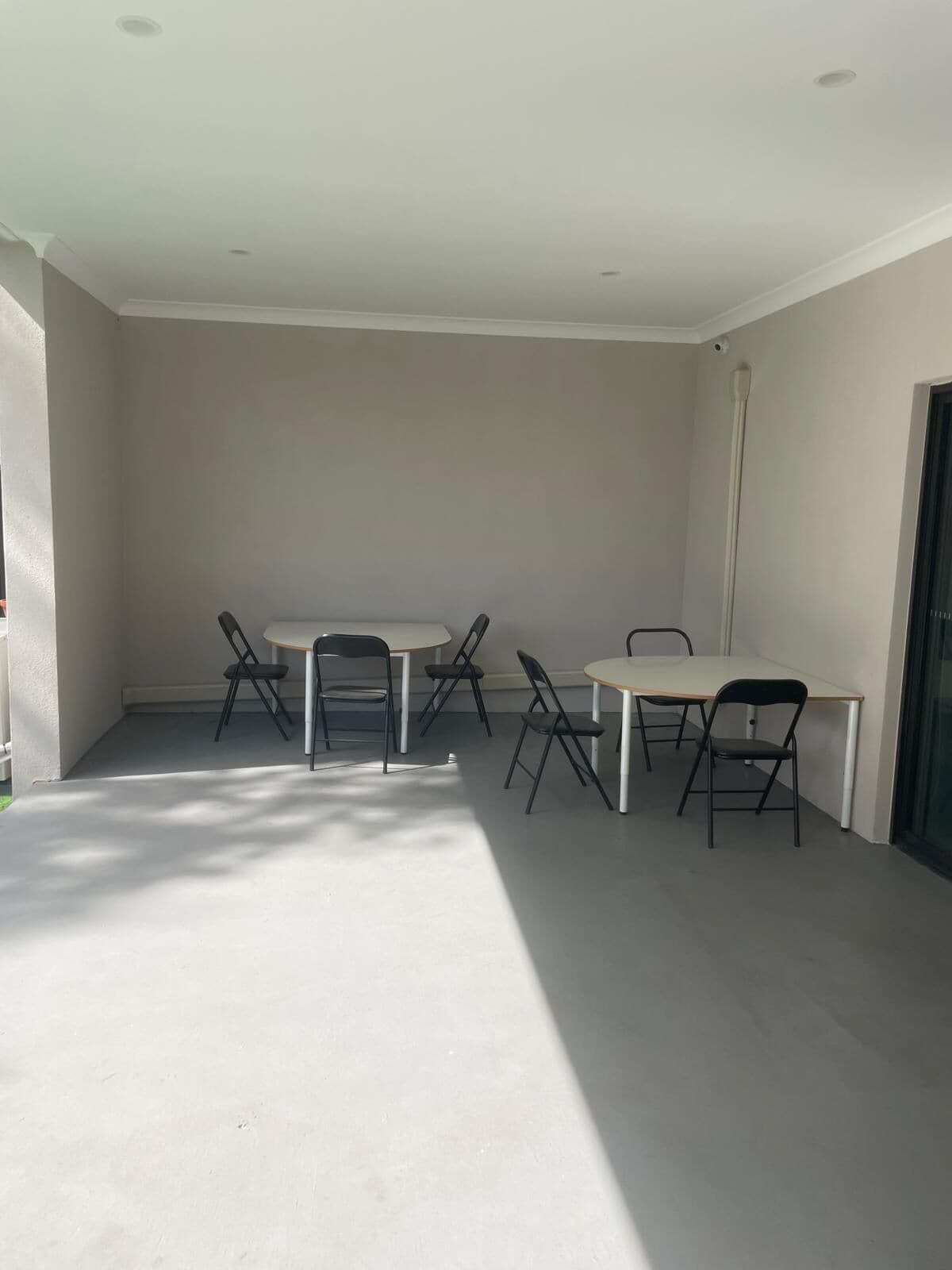 A room with a white ceiling, recessed lighting, a white table with four chairs, and a glass door on the right.