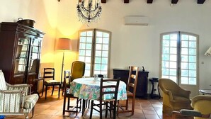 A dining area with a chandelier, wooden chairs, a table with a tablecloth, and a cabinet. - Family home with large pool in Provence (Saint-Mitre-les-Remparts)