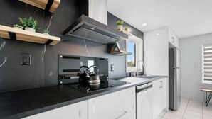 A modern kitchen with a black countertop, white cabinets, a built-in stove, and a stainless steel range hood. - SPA | Entre fleuve et montagne | Chalet La Shred (Petite-Rivière-Saint-François)