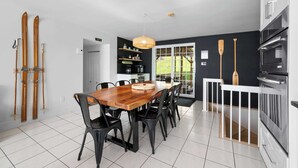 A modern kitchen with a wooden dining table, black chairs, and a hanging light fixture. - SPA | Entre fleuve et montagne | Chalet La Shred (Petite-Rivière-Saint-François)