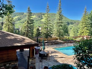 A pool area with a wooden deck, stone patio, and a view of a mountainous landscape. - Vail Condo Near Gondola with Mtn Views, SV12E (Vail)