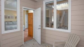 Une pièce avec une grande fenêtre, une porte en bois et une chaise en plastique blanche.