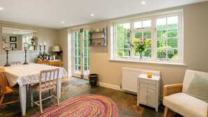 A dining area with a table set for four, a radiator, a window with a view of greenery, and a chair with a cushion. - Lovely 5BD Home with Cinema & Games Room (Marsh Gibbon)