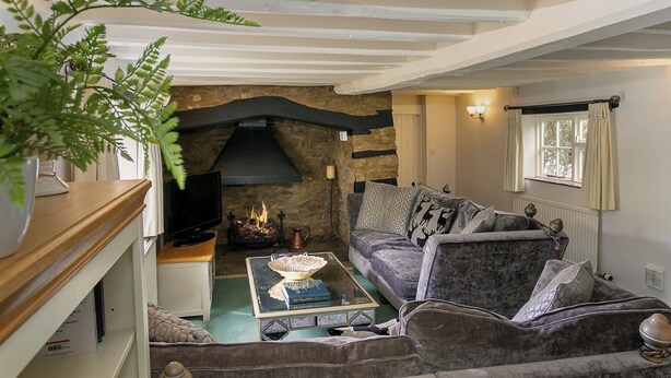 A cozy living room with a stone fireplace, a comfortable sofa, and a television on a wooden stand. - Lovely 5BD Home with Cinema & Games Room (Marsh Gibbon)