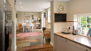 A kitchen with a clock, a chalkboard, and a dining area with chairs and a table. - Lovely 5BD Home with Cinema & Games Room (Marsh Gibbon)