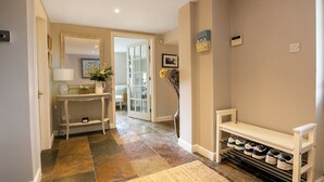A hallway with a tiled floor, a bench, a shoe rack, and a door leading to another room. - Lovely 5BD Home with Cinema & Games Room (Marsh Gibbon)