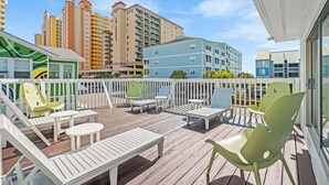 A wooden deck with white and green lounge chairs, a small table, and a white fence. - Sunny 3BR Near the Beach at Palm Court  (#17) (North Myrtle Beach)
