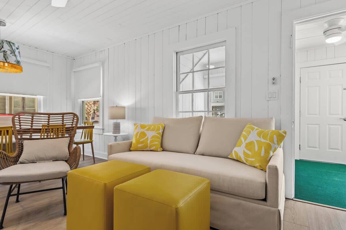 A living room with a beige sofa, yellow ottomans, and a wicker chair.