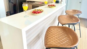Een moderne keuken met een wit aanrecht, donkere kastjes en een roestvrijstalen koelkast. Er staan twee barkrukken en een glas sinaasappelsap op het aanrecht.