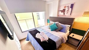 Een moderne slaapkamer met een bed, nachtkastje, televisie en raam.