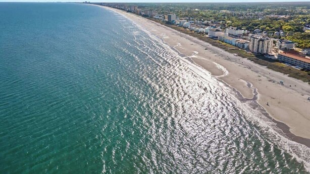 Un paisaje costero con una playa extensa, edificios a lo largo de la costa y cielo despejado.