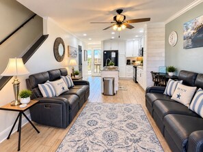 A modern living room with leather sofas, a patterned rug, and a ceiling fan. - Captain Chris at South Winds | Across from Beach + Walk to Gulf Shores Fun (Gulf Shores)