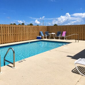 Ein Schwimmbad mit Holzumzäunung, Liegestühlen und einem Tisch.