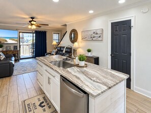 A modern kitchen with a marble countertop, a built-in dishwasher, and a view to the outside. - Captain Chris at South Winds | Across from Beach + Walk to Gulf Shores Fun (Gulf Shores)
