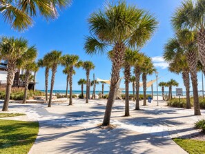 A beachfront promenade with palm trees, a star-shaped sculpture, and a public beach access sign. - Captain Chris at South Winds | Across from Beach + Walk to Gulf Shores Fun (Gulf Shores)