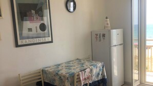 A room with a bed, a table with a tablecloth, a refrigerator, a clock, and a framed picture on the wall. - House by the sea (Lido Chiatona-Stazione di Palagiano)