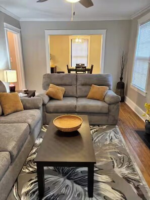 Ein Wohnzimmer mit einem grauen Ecksofa, einem Holztisch und einem gemusterten Teppich.