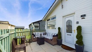 A white house with a number 12 sign, a front porch with a bench and chairs, and a small table. - Beachfront Chalet – Detached, Sleeps 6, Pet-Friendly, Heating Included, Wifi (Wilsthorpe)