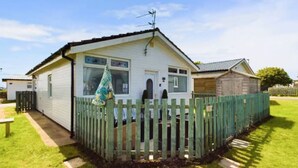 A mobile home with a fenced backyard, a small porch, and a window with a curtain. - Beachfront Chalet – Detached, Sleeps 6, Pet-Friendly, Heating Included, Wifi (Wilsthorpe)