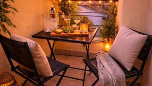 En balkon med to stole, et bord med drikkevarer og lyskæder.
