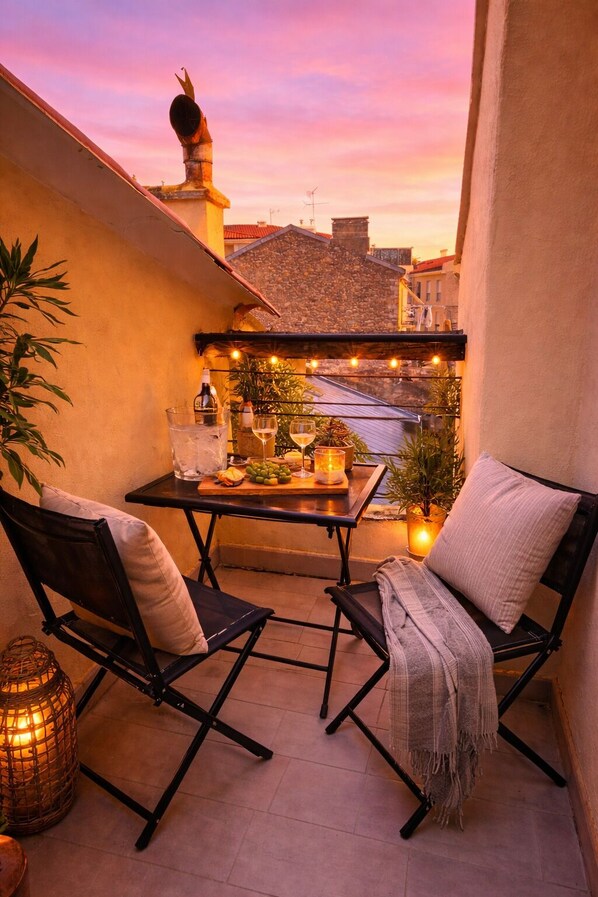 A balcony with two chairs, a table with drinks, and string lights.