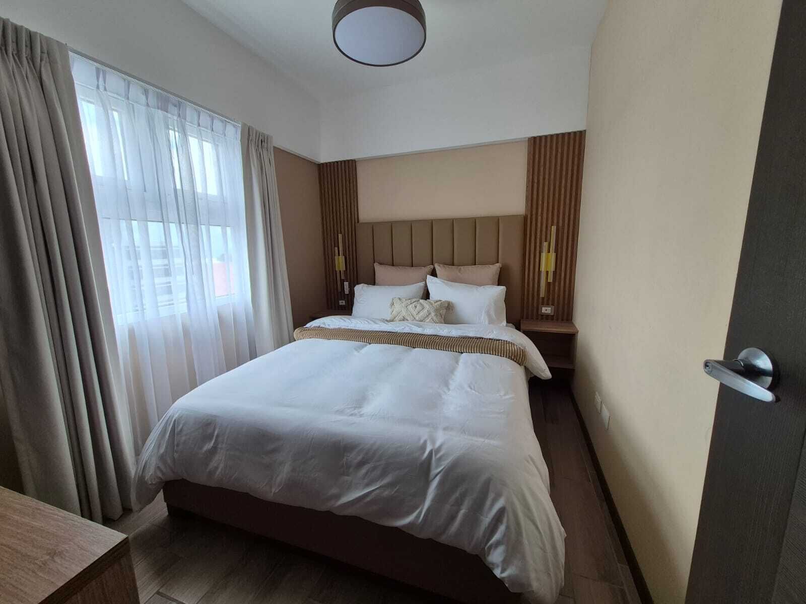 Ein Hotelzimmer mit einem großen Bett, einem Nachttisch und einem Fenster mit Vorhängen.