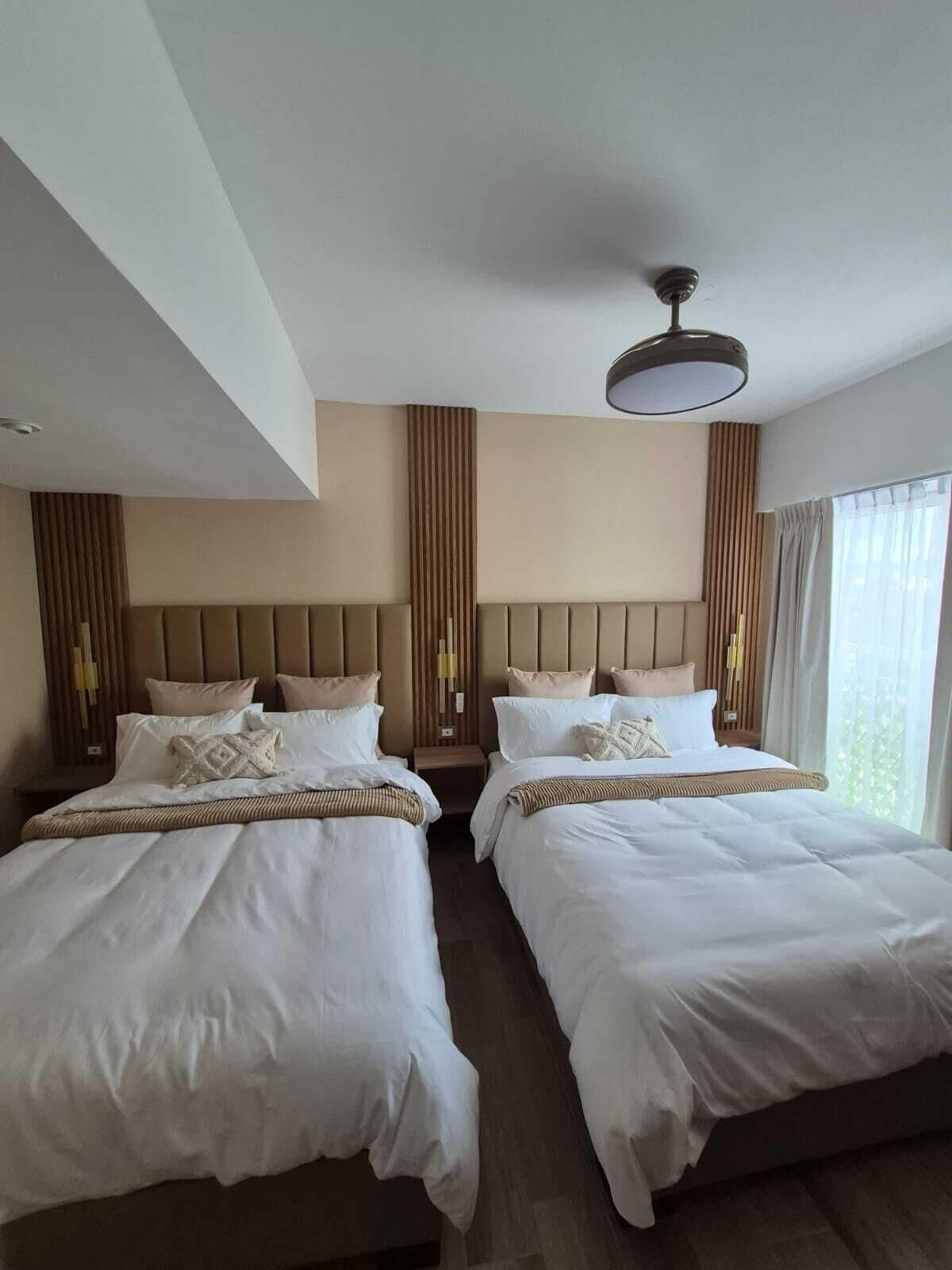 A hotel room with two beds, a ceiling fan, and a large window.