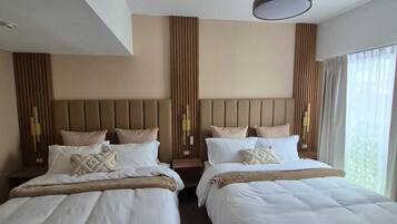 A hotel room with two beds, a ceiling fan, and a large window.