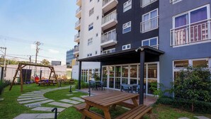 Une cour avec une table de pique-nique, une balançoire et un bâtiment doté de balcons.