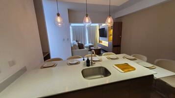 A modern kitchen with a central island, pendant lighting, and a view into a living area.