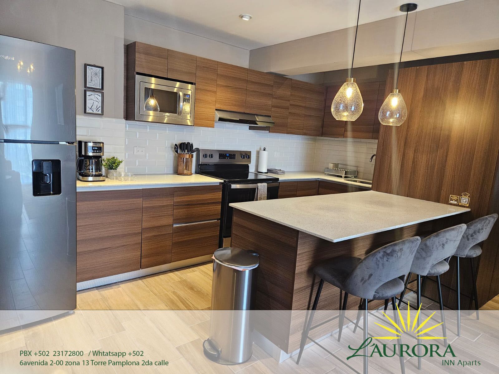 A modern kitchen with wooden cabinets, stainless steel appliances, a central island, and pendant lighting.