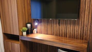 A modern room with a wooden panel wall, a flat-screen TV mounted above a wooden desk, a small stool, and a potted plant.