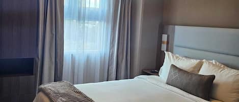A hotel room with a large bed, a headboard, a bedside table, and a ceiling light fixture.