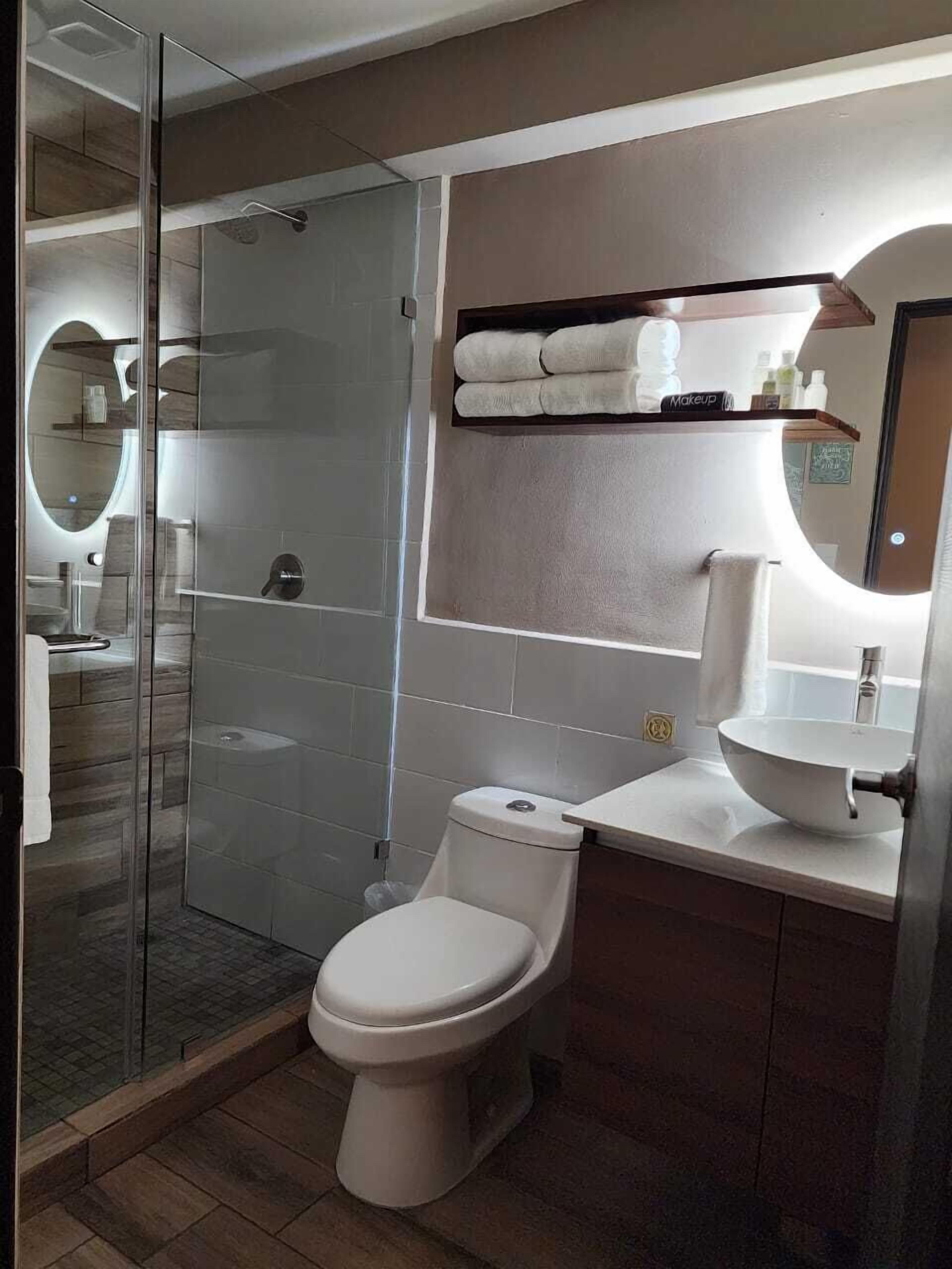 Un baño moderno con cabina de ducha de vidrio, inodoro, lavabo y tocador con espejo.