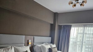 Une chambre d’hôtel avec deux lits, une grande fenêtre avec des rideaux, un lustre moderne et une vue sur la ville.