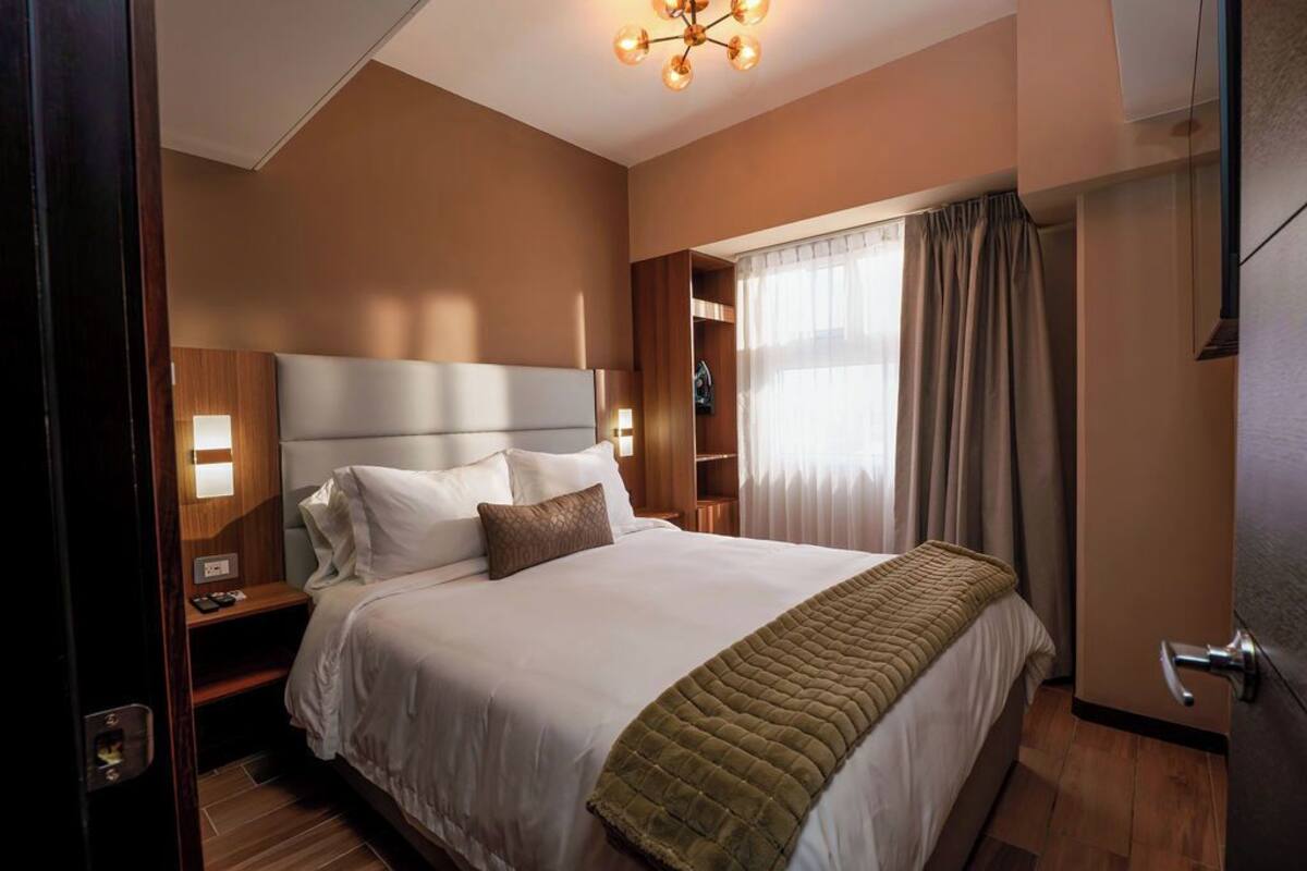Una habitación de hotel con una cama grande, mesitas de noche, un armario y una ventana con cortinas.