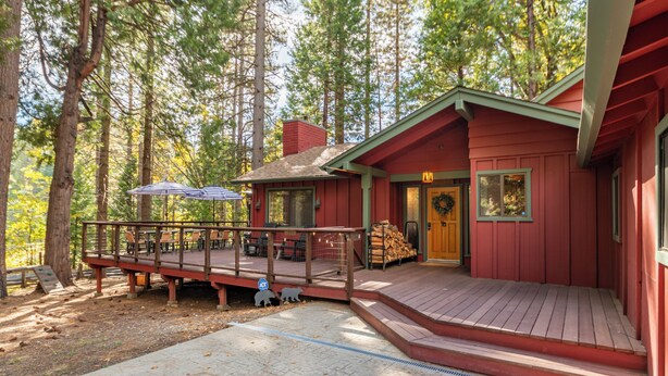 Uma cabana vermelha com um deck de madeira, área de estar externa e um espaço coberto com guarda-sóis.