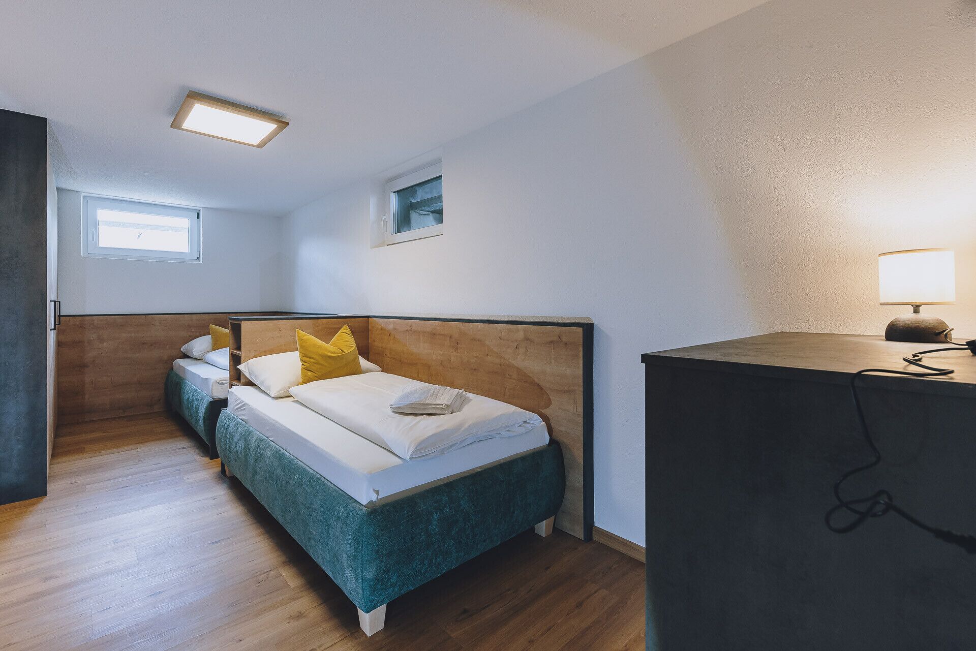 Une chambre à coucher avec une tête de lit en bois, un lit recouvert de draps blancs, une petite fenêtre et un bureau avec une lampe.