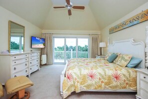 Quarto com cama, penteadeira, televisão e varanda com cortinas.