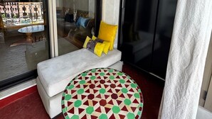 Ein Balkon mit einer Couch, einem Tisch mit Muster und einem schwarzen Kleiderschrank.