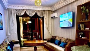 Ein geräumiges Wohnzimmer mit rundem Couchtisch, einer Sofagarnitur, einem an der Wand befestigten Fernseher und einer dekorativen Stehlampe.