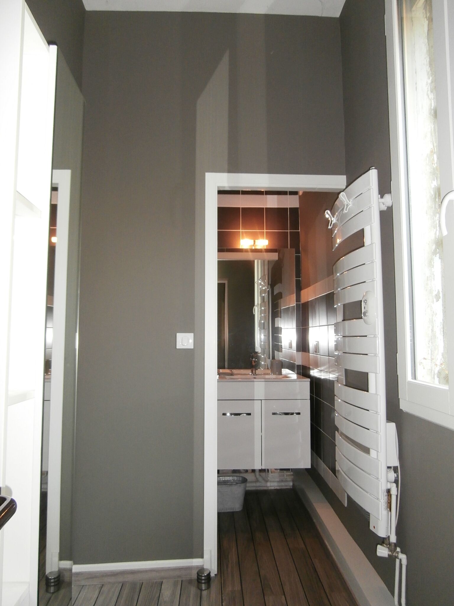 A narrow bathroom with a mirror, a radiator, and a sink.