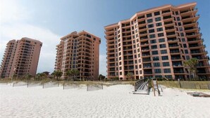 Tres edificios altos con balcones, situados en una playa arenosa.