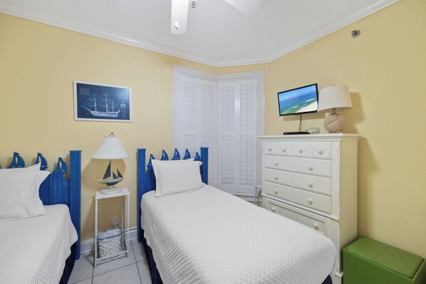 A hotel room with two beds, a television, a dresser, a green bench, and a sailboat decoration. - SeaChase 702C by Liquid Life (Orange Beach)