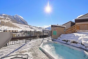 A snow-covered outdoor area with a hot tub, wooden deck, and a view of mountains. - Snowcrest Classic Crested Butte! 2 Bed, 2bath (Crested Butte)