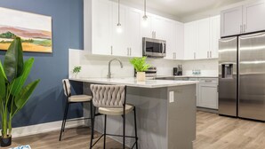 Una cocina moderna con armarios blancos, electrodomésticos de acero inoxidable y un taburete de bar.