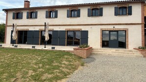 A two-story house with a tiled roof, multiple windows with shutters, and a gravel driveway. - Le Clos de Galou, Authenticity, Comfort, Nature (Aucamville)