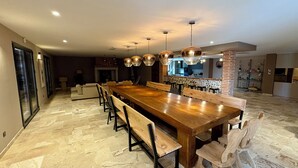 A spacious dining area with a long wooden table and benches, a kitchen in the background, and a stone-tiled floor. - Le Clos de Galou, Authenticity, Comfort, Nature (Aucamville)