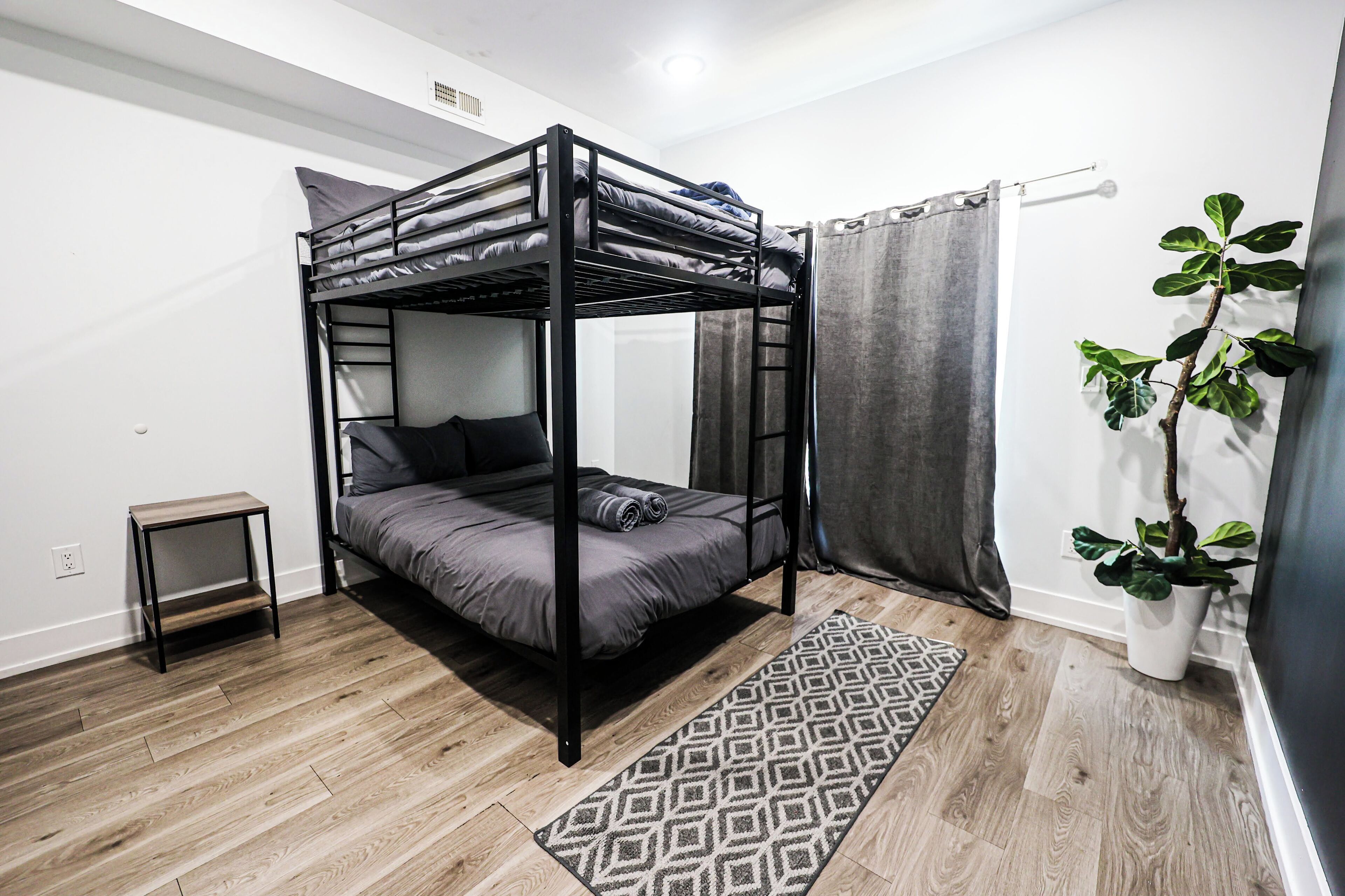 A bunk bed room with a small side table, a patterned rug, and a potted plant.