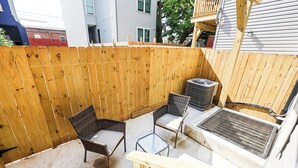En terrasse med træhegn, to fletstole, et glasbord og en grill.